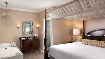 A hotel room with a large bed, a separate bathroom with a bathtub, a vanity with a mirror, and a chandelier.