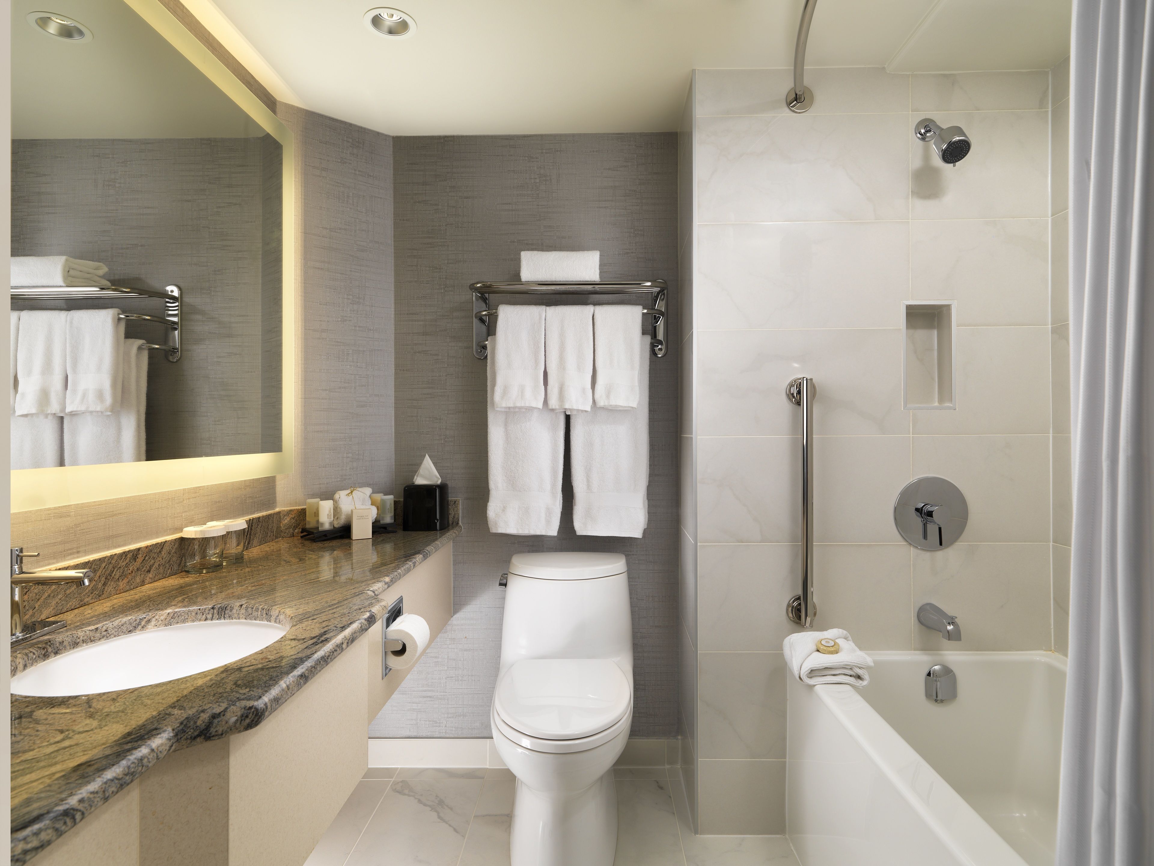 A modern bathroom with a marble countertop, a toilet, a shower with a handheld showerhead, and a bathtub.
