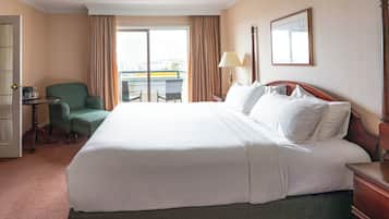 A hotel room with a large bed, a chair, a desk, a lamp, and a window with curtains.
