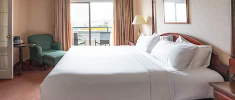 A hotel room with a large bed, a chair, a desk, a lamp, and a window with curtains.