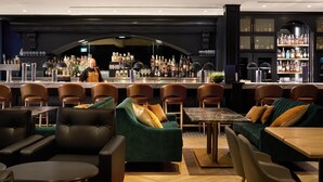 Un espace bar avec des fauteuils en cuir, un comptoir et des étagères remplies de bouteilles d’alcool.