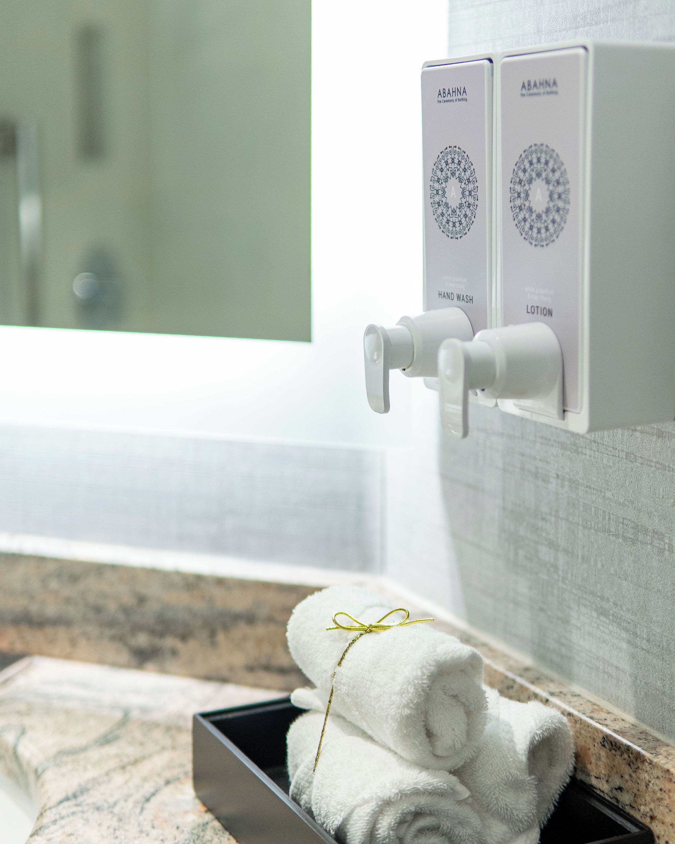 Une salle de bain équipée d’un distributeur de savon liquide et de lotion, d’un porte-serviettes avec des serviettes pliées, et d’un miroir qui reflète la pièce.