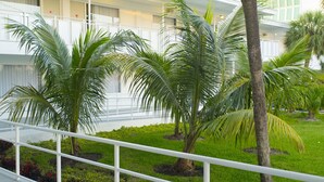 Un hotel con balcón, palmeras y un césped bien cuidado.