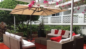 Un patio amueblado con mobiliario de mimbre, incluyendo sofás y una mesa de centro, bajo un paraguas grande.