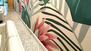 Un pasillo con un mural de hojas tropicales, un banco blanco y un suelo moteado.