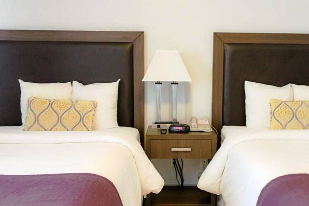 A hotel room with two beds, each with a headboard, a bedside table with a lamp, and a phone.