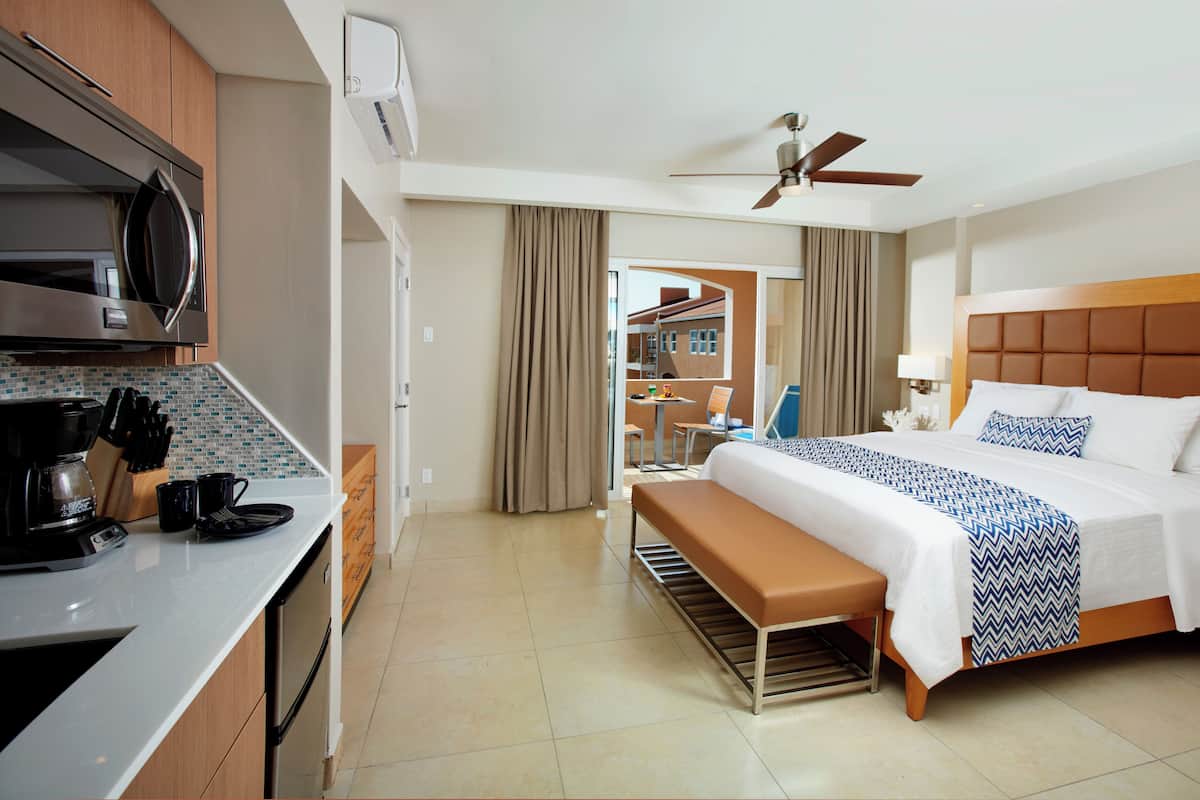 A hotel room with a bed, a bench, a kitchenette, and a view of the outside.