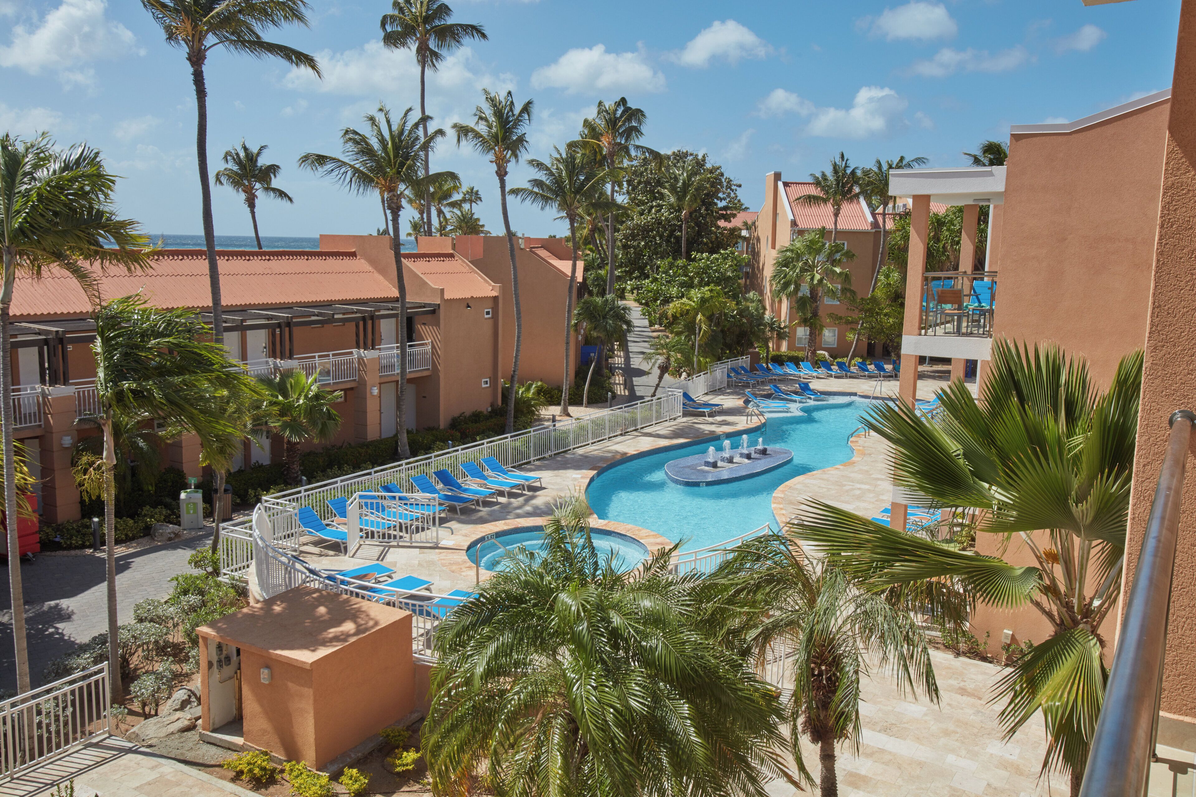 A resort with multiple swimming pools, palm trees, and a view of the ocean.