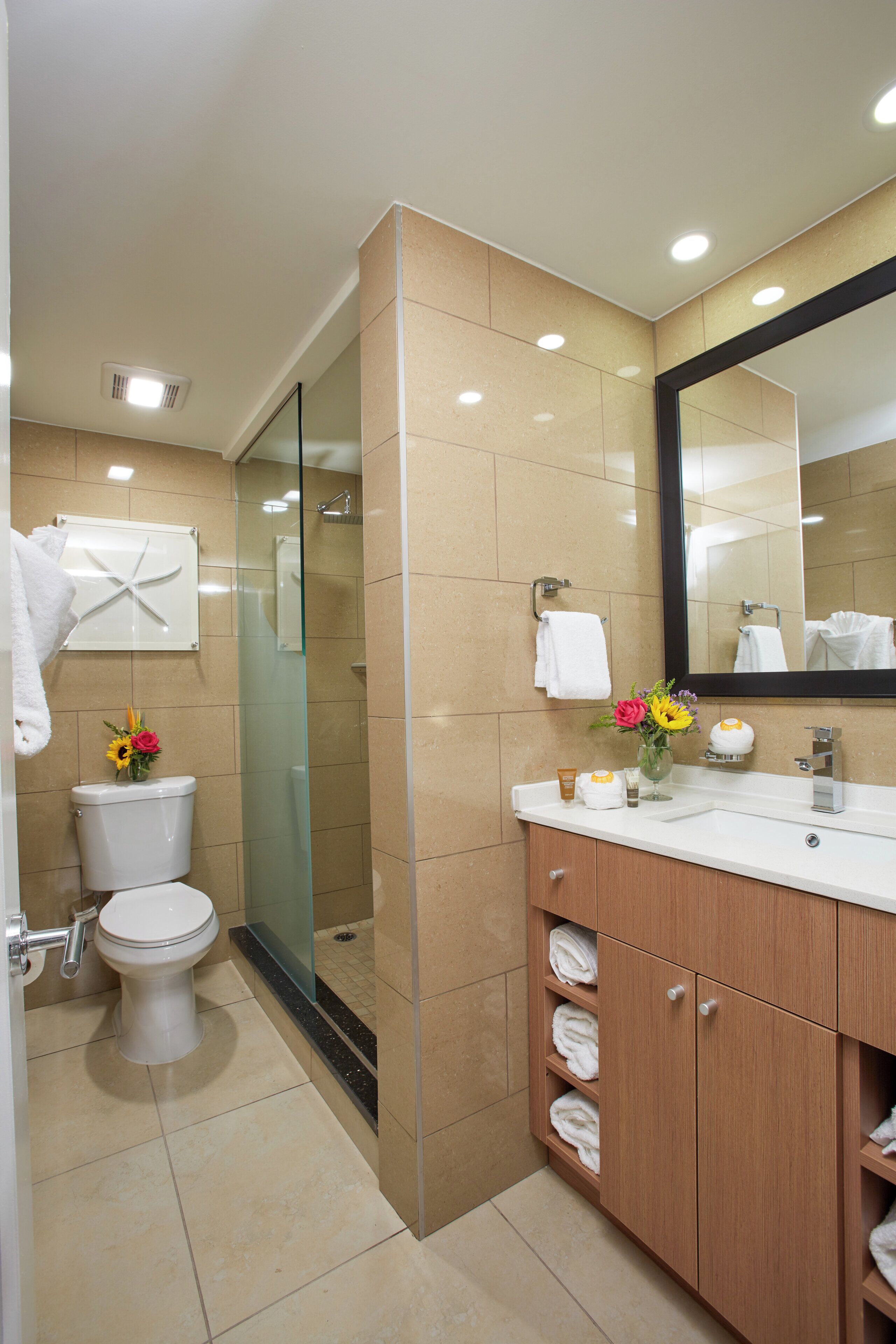 Une salle de bain comprenant des toilettes, un espace de douche vitré, un lavabo avec un miroir et un meuble-lavabo avec des étagères pour les serviettes.