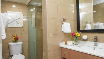 A bathroom with a toilet, a glass shower enclosure, a sink with a mirror, and a vanity with shelves for towels.