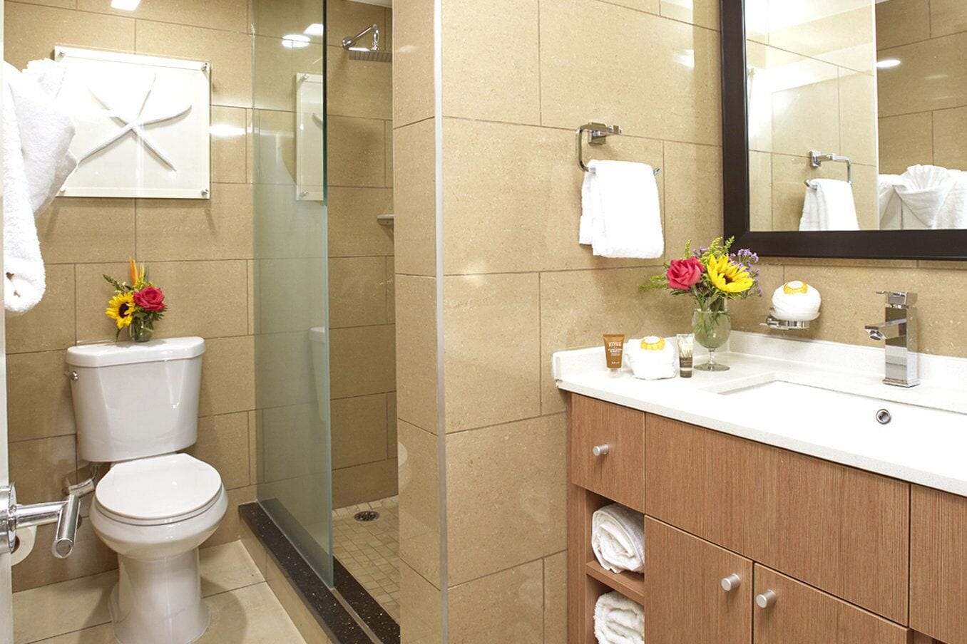 Un baño con inodoro, cabina de ducha de vidrio, lavabo con artículos de aseo personal y un espejo.