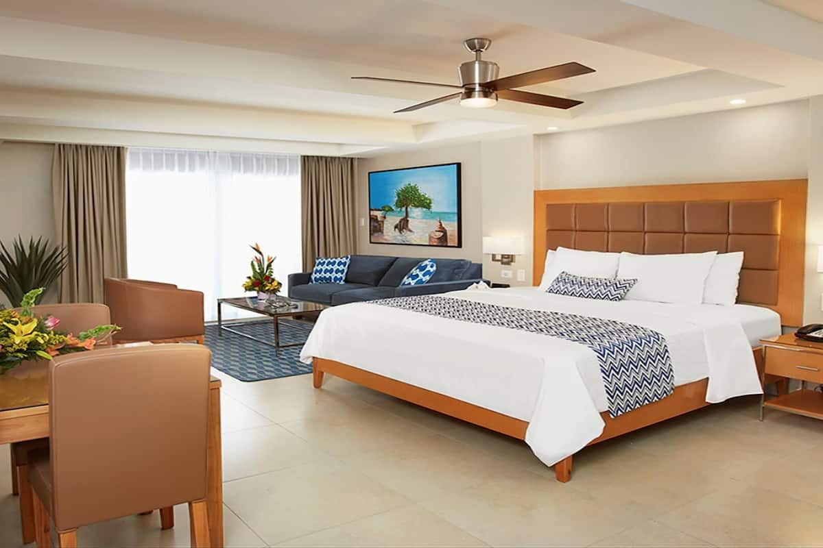 A hotel room with a bed, a desk, a chair, a television, and a ceiling fan.