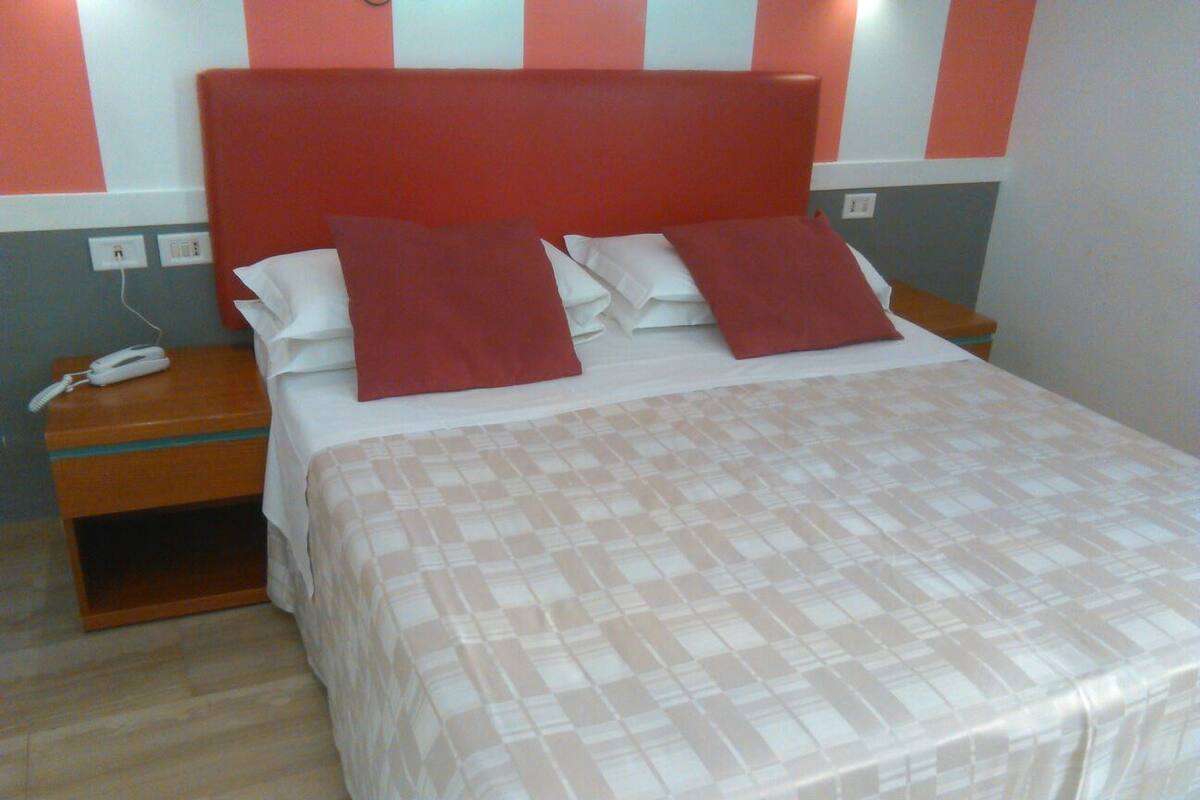 A neatly made bed with a checkered bedspread, a wooden nightstand with a phone, and a red headboard.