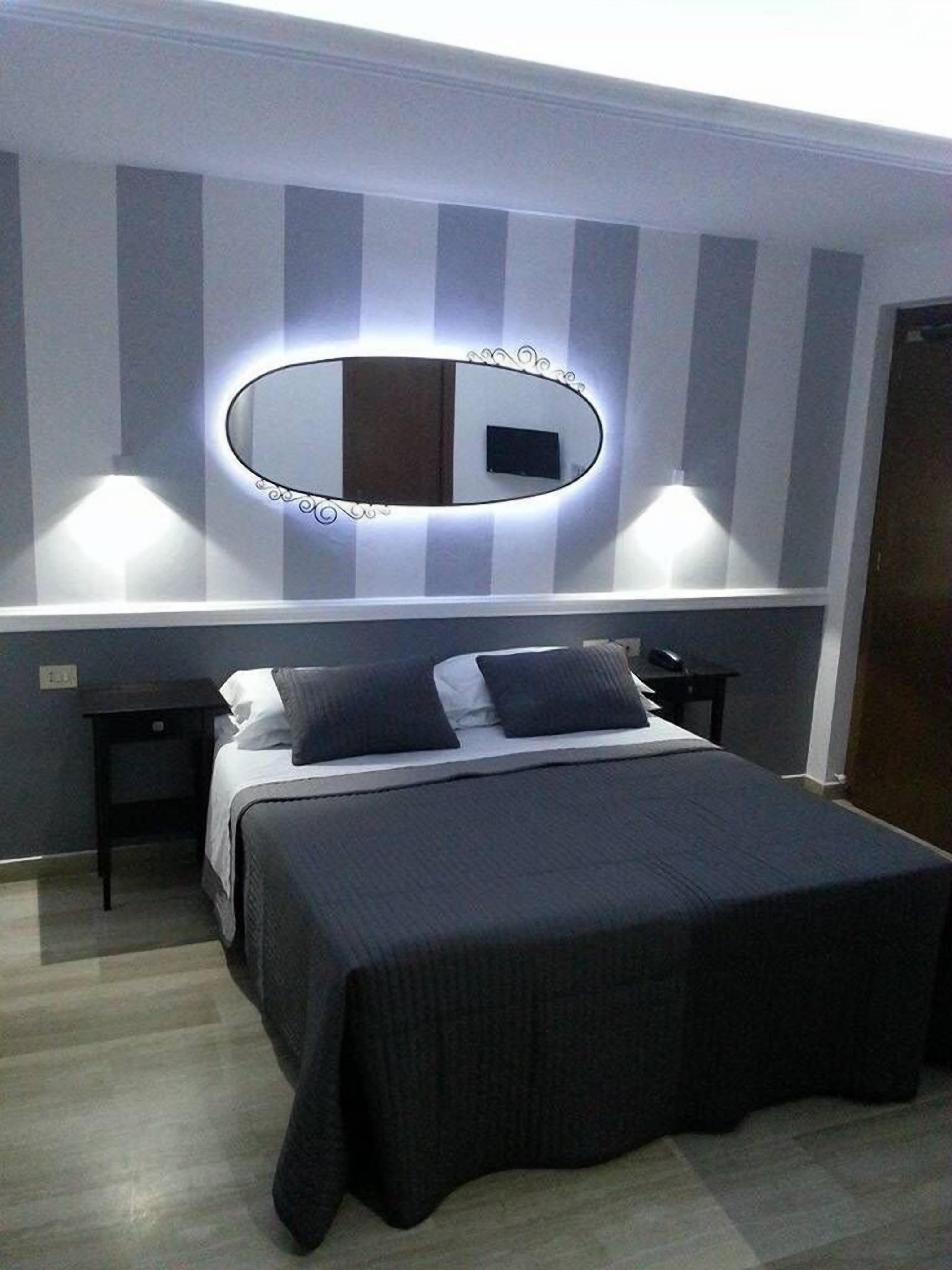 A hotel room with a bed, bedside tables, a mirror, and a wall-mounted light fixture.