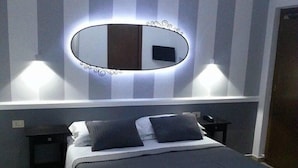 Un dormitorio moderno con una cama grande, una mesita de noche, un espejo en la pared y un televisor.