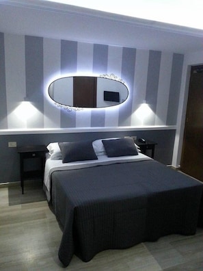 A modern bedroom with a large bed, a bedside table, a nightstand, a wall-mounted mirror, and a TV. - Hotel Center 1 (Rome)