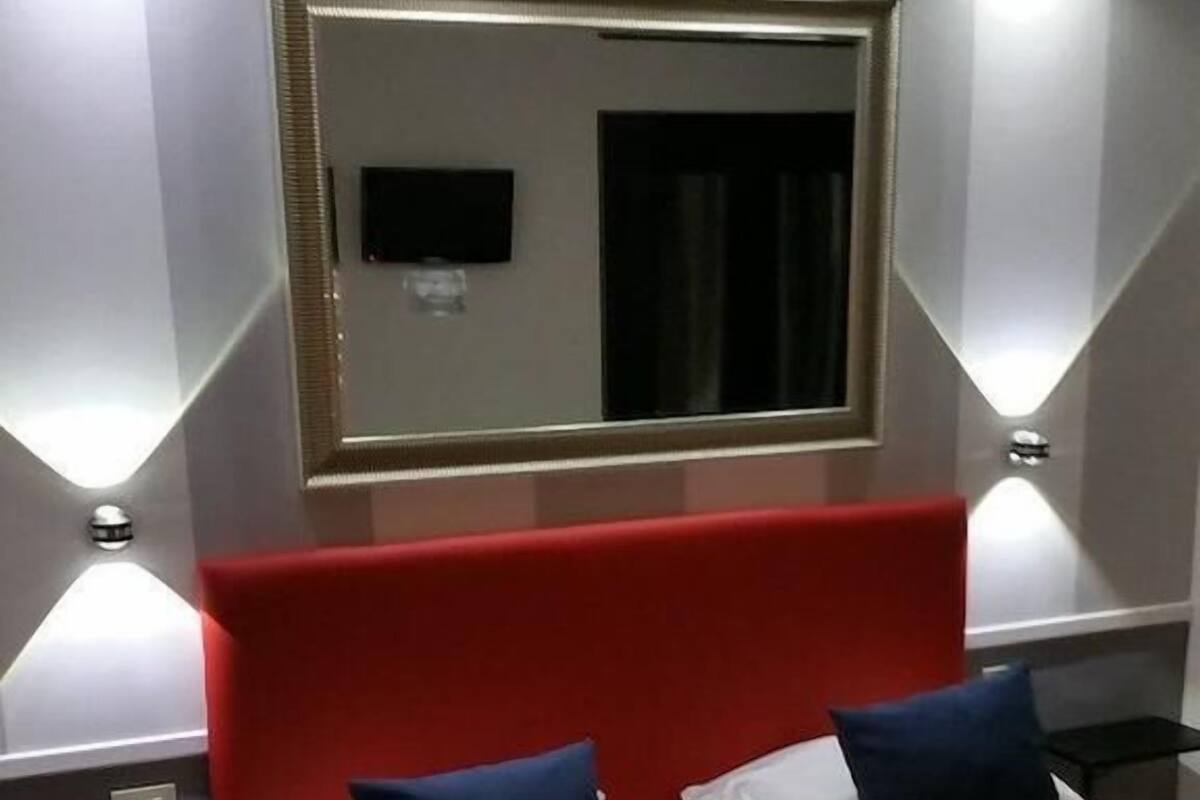 A hotel room with two single beds, a red headboard, and a large mirror above the beds.