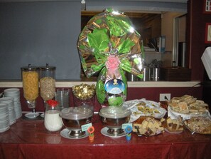 Una mesa de buffet con diversos alimentos y recipientes, incluyendo un gran regalo envuelto y platos etiquetados.