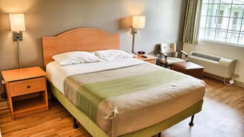 Una cama bien hecha con cabecera de madera, dos mesitas de noche, una silla, un calentador y una ventana con cortinas.