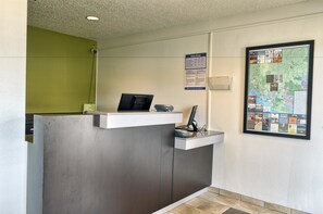Reception area with a flat-screen monitor, keyboard, and mouse at the central desk, surrounded by a green accent wall and a large informational poster.