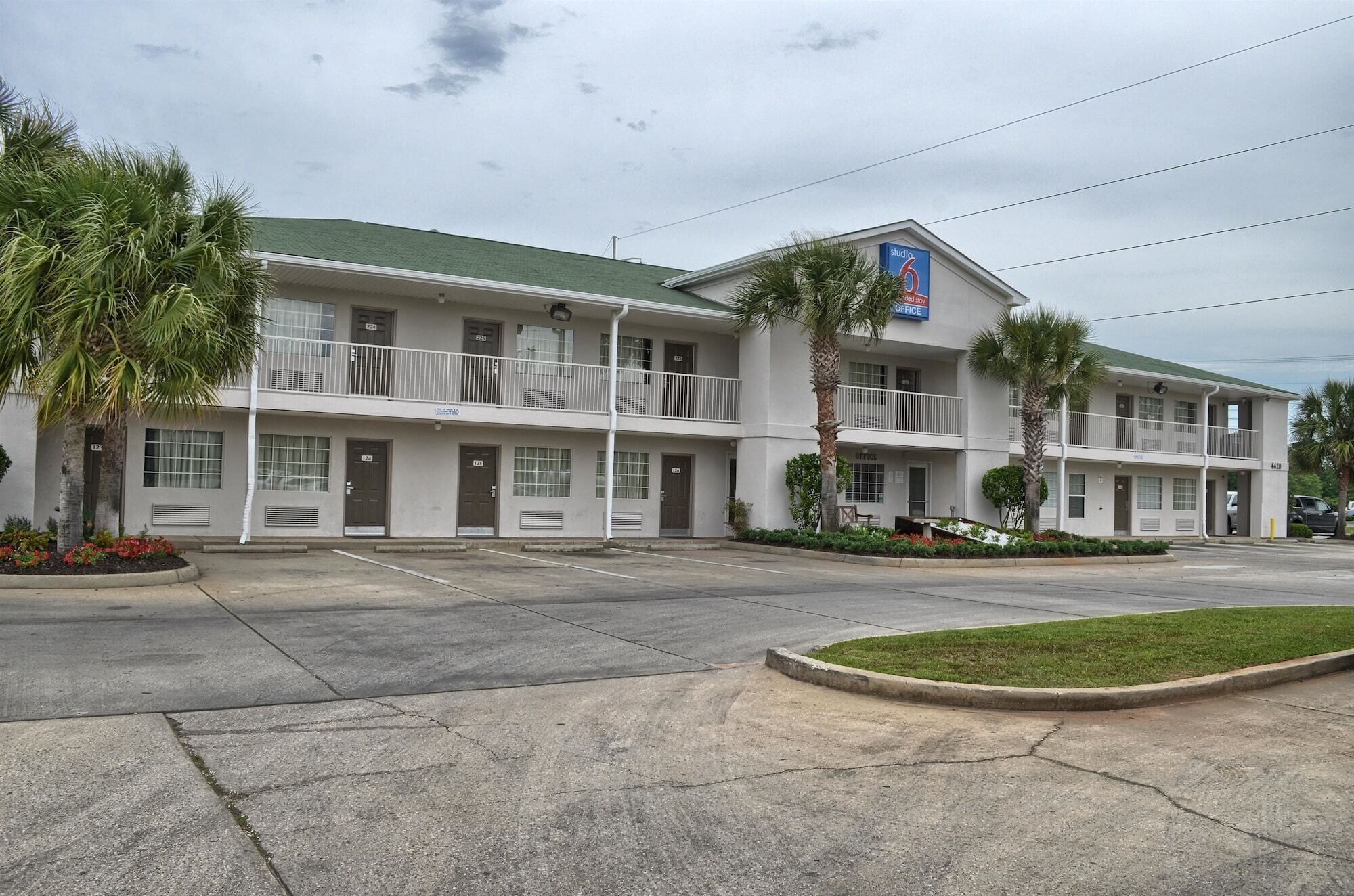 A motel with a two-story structure, multiple balconies, and a parking lot in front.
