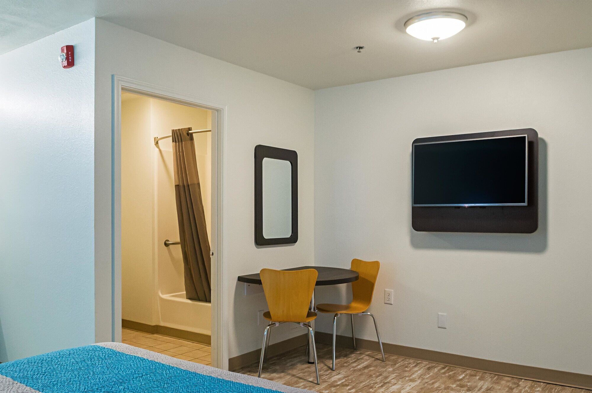 A hotel room with a shower, a small table with two chairs, a flat-screen TV mounted on the wall, and a mirror.