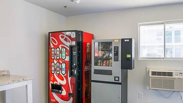 Ein Zimmer mit einem Coca-Cola-Automaten, einer Minikühlschrank und einem Fenster mit Jalousien.