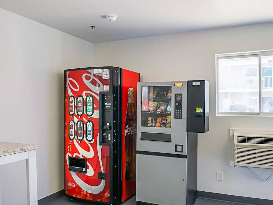 Ein Zimmer mit einem Coca-Cola-Automaten, einer Minikühlschrank und einem Fenster mit Jalousien.