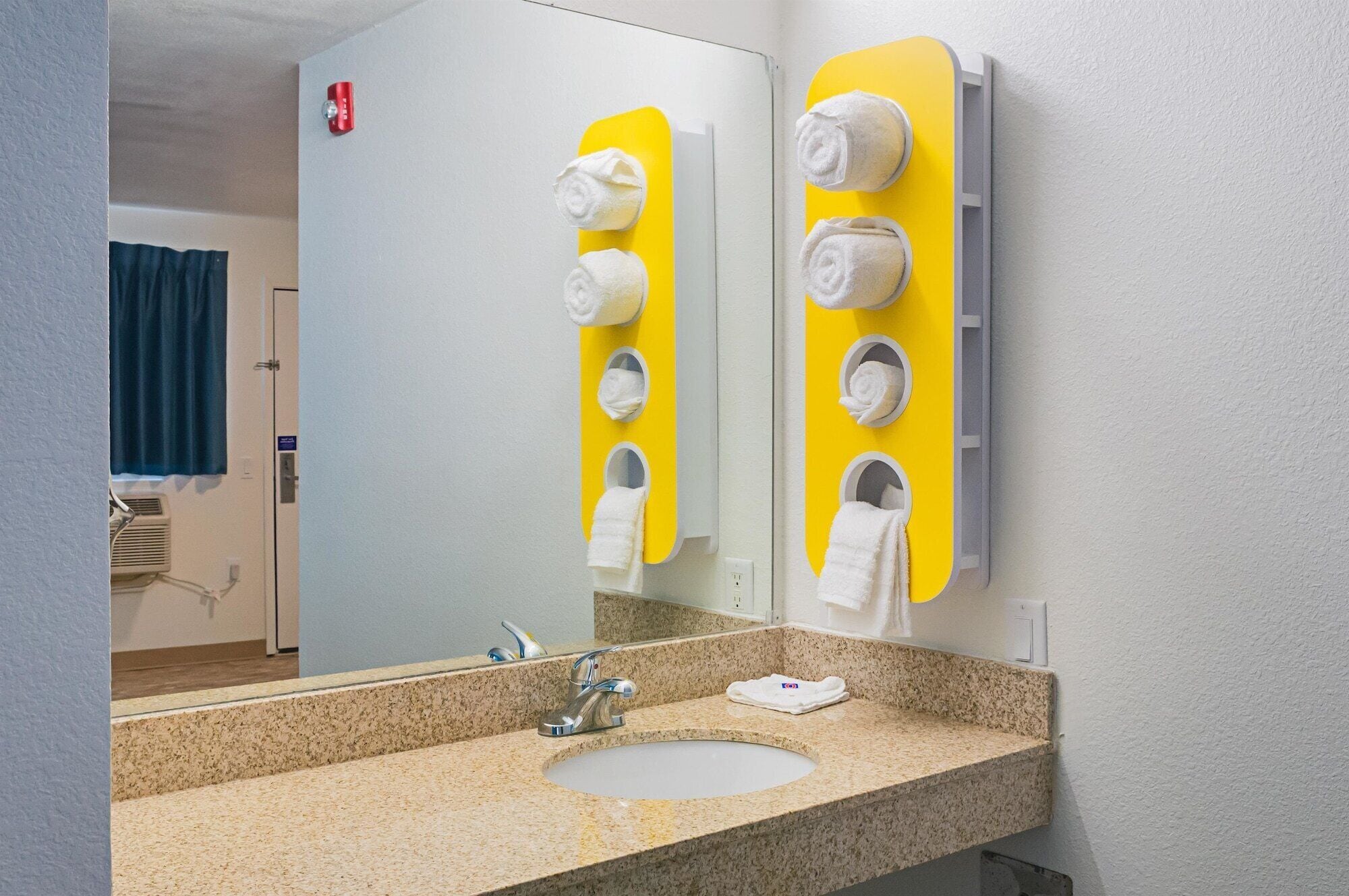 A bathroom with a granite countertop sink, a mirror, and a yellow towel dispenser with multiple slots.
