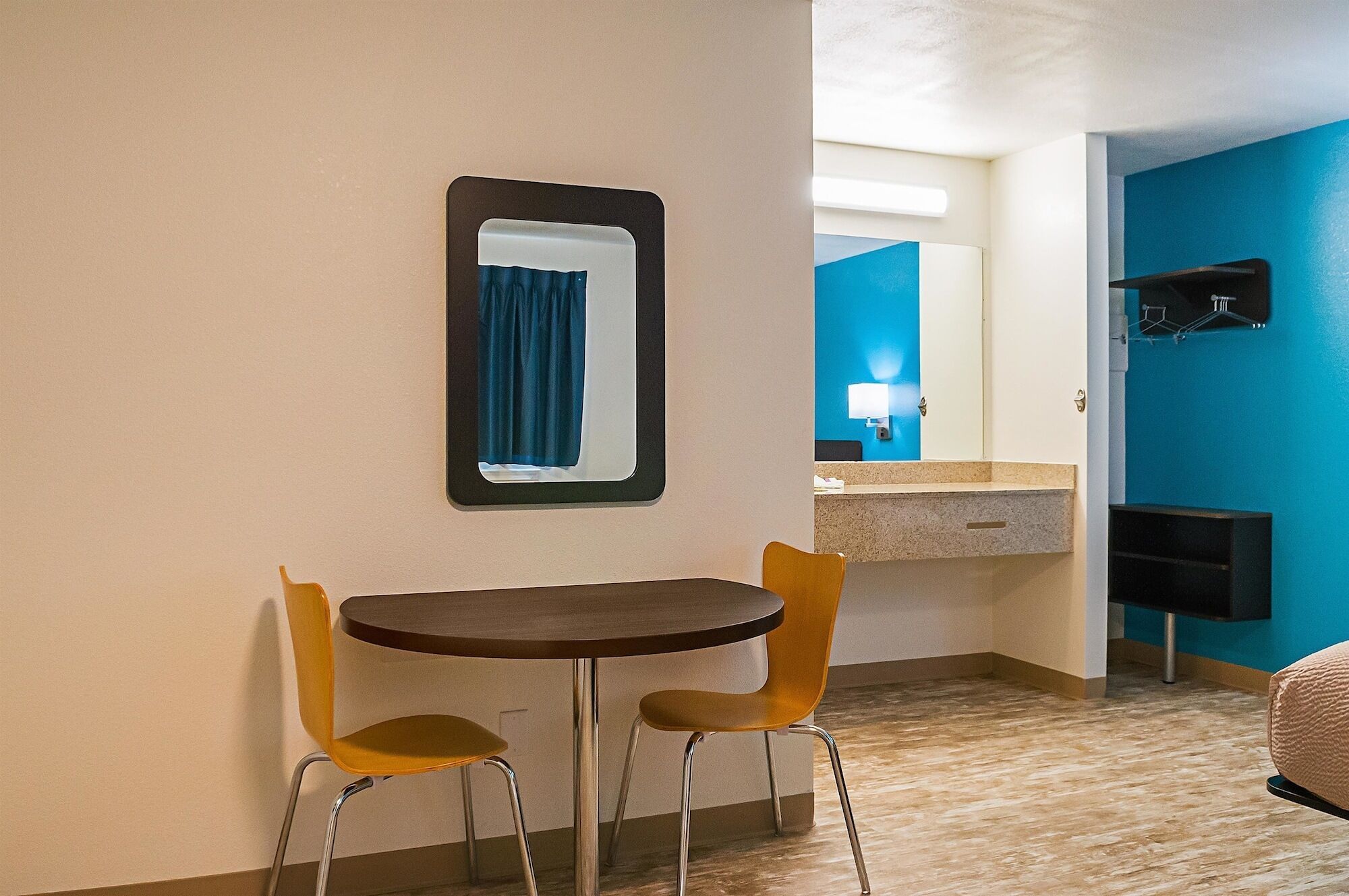 A small room with a round table and two chairs, a mirror on the wall, and a bathroom with a blue wall and a sink.