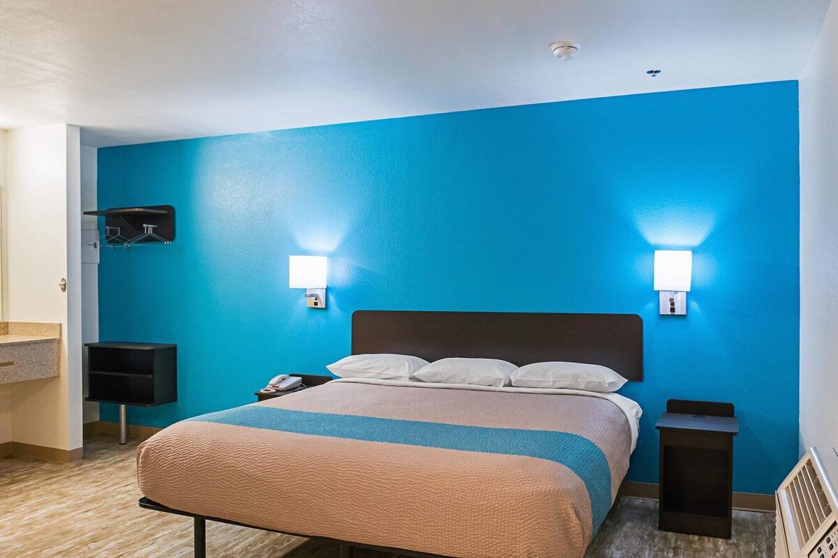 Ein Hotelzimmer mit Bett, Nachttisch, fest installiertem Telefon und Wandleuchte.