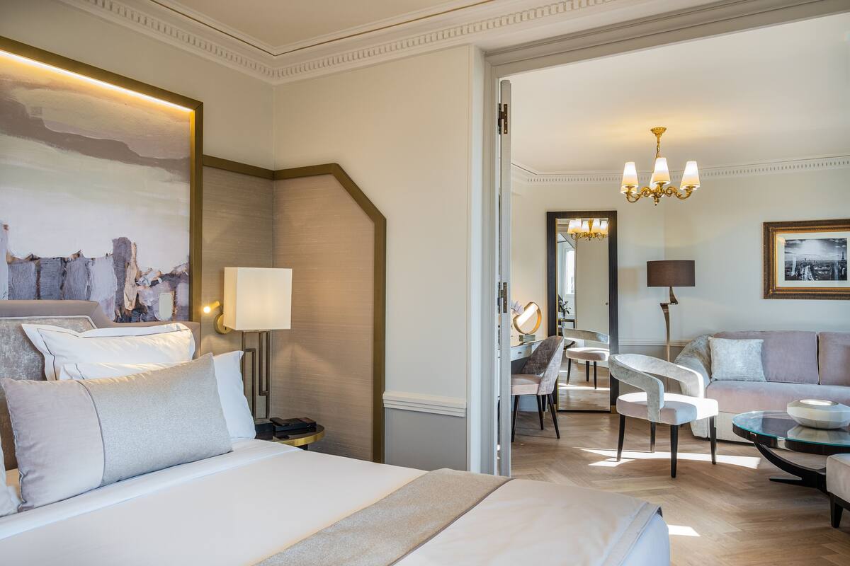 A hotel room with a large bed, a desk with a chair, a sofa, and a chandelier.