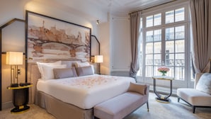 A hotel room with a large bed, a bench, a bedside table, a nightstand, a window with curtains, and a painting on the wall. - Hôtel Elysia by Inwood Hotels (Paris)