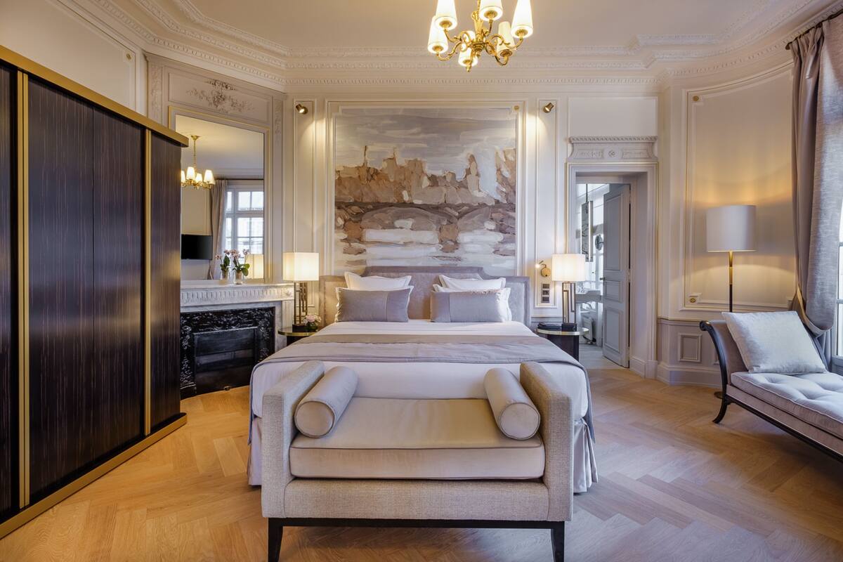 A spacious bedroom with a large bed, a sofa, a fireplace, and a cityscape mural on the wall.