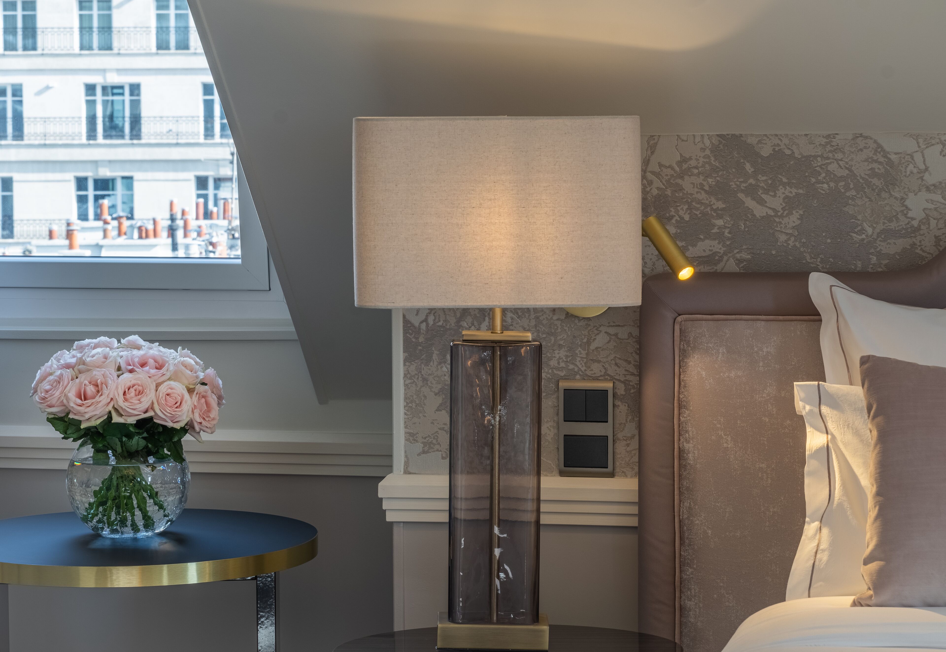 Une chambre d’hôtel avec un lit, une table de chevet avec une lampe et un vase de fleurs.