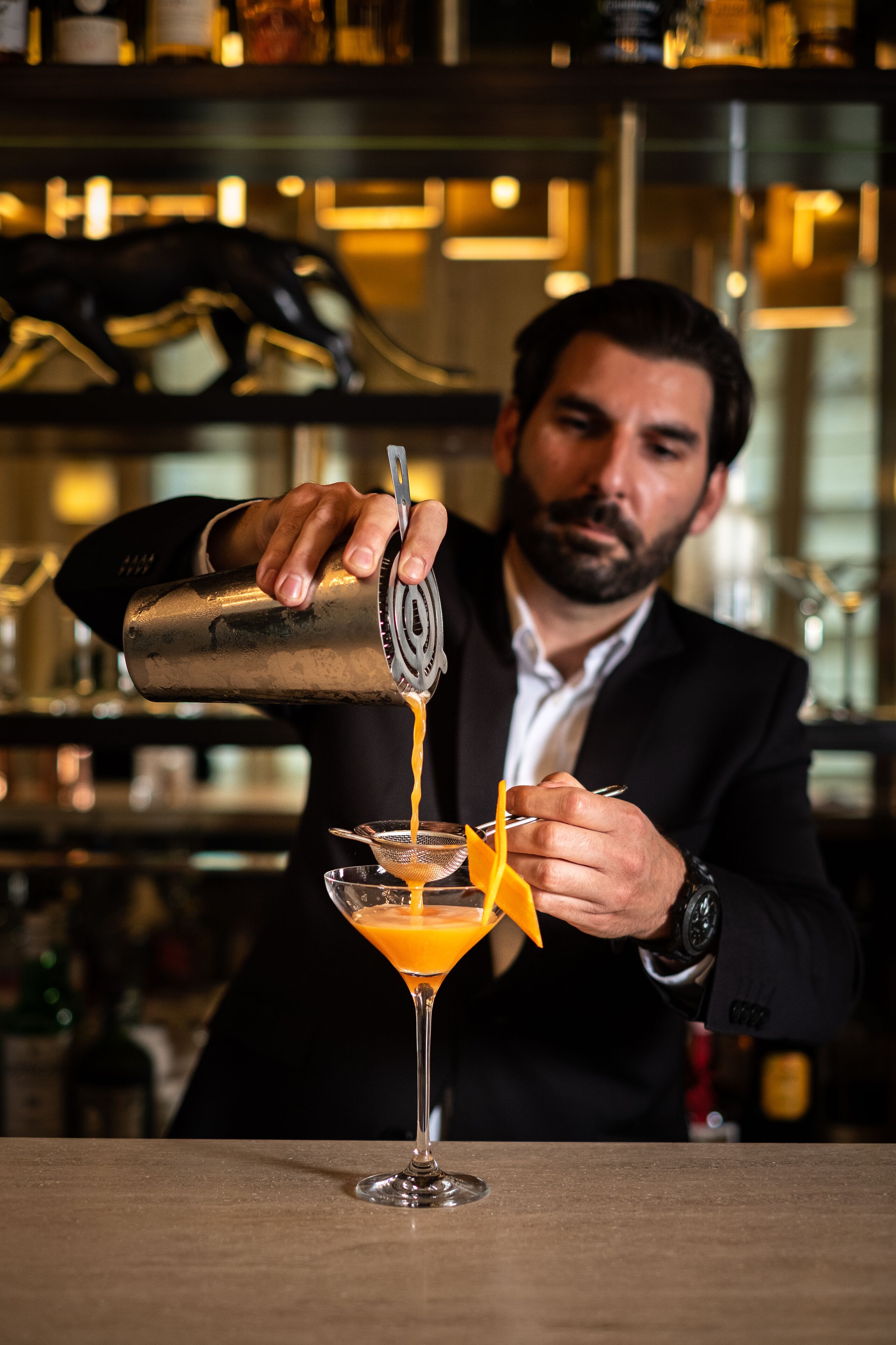 A bartender pouring a drink into a martini glass.