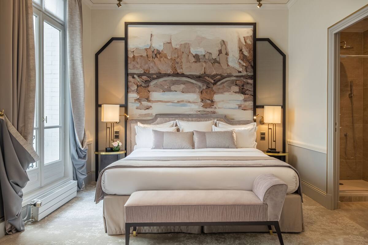 A bedroom with a large bed, bedside lamps, a bench, and a large abstract painting on the wall.