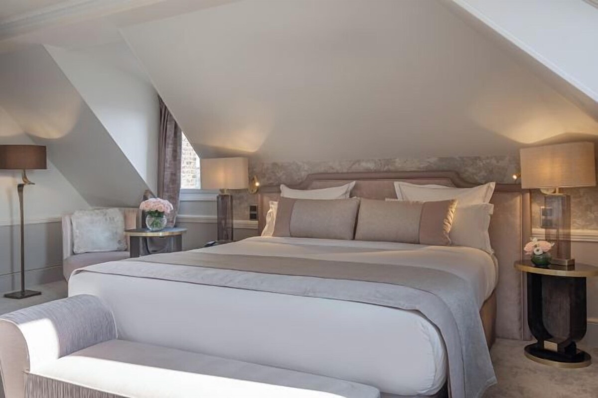 A bedroom with a large bed, two bedside tables, a nightstand, and a small round table with a lamp.