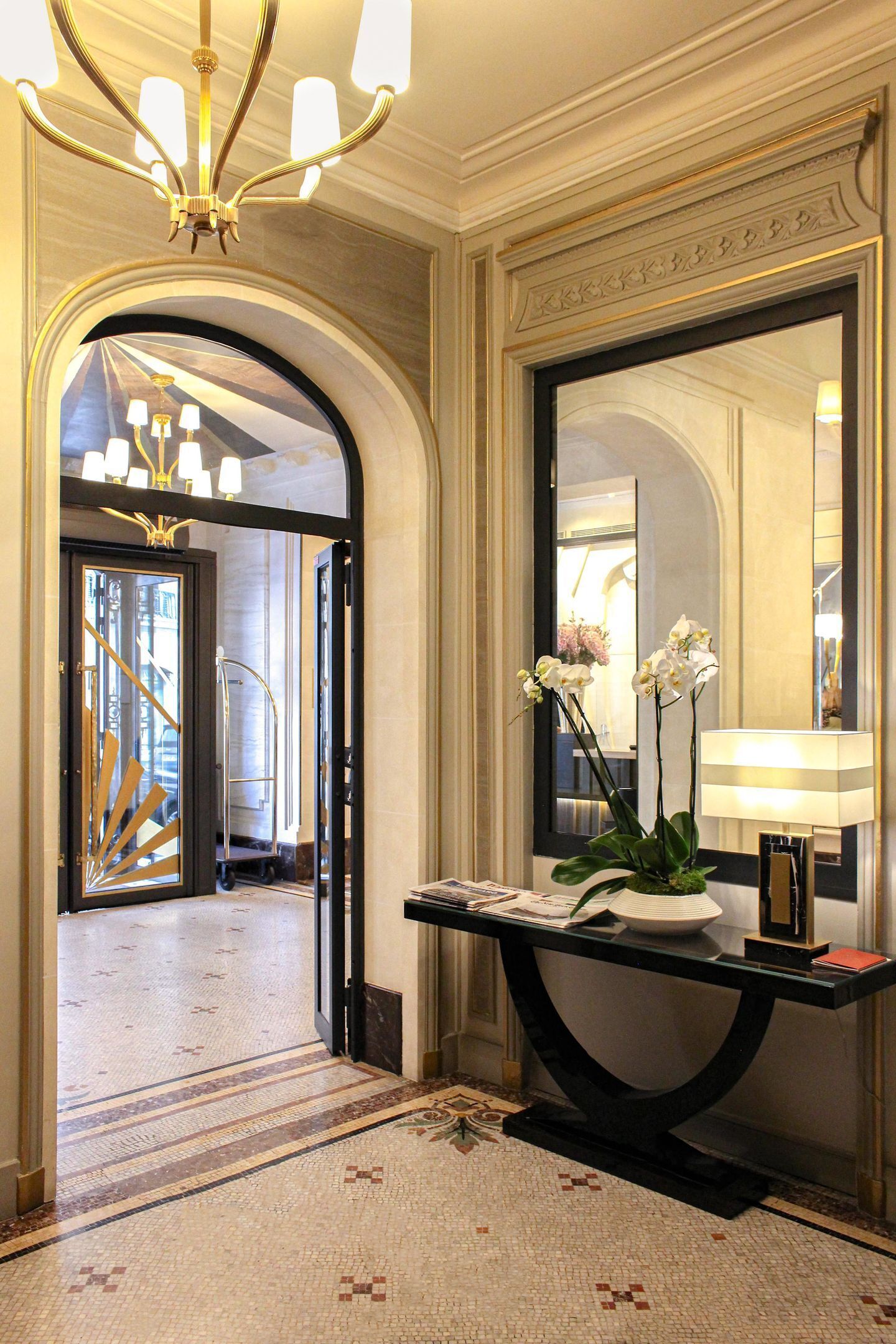 A lobby with a reception desk, a chandelier, a mirror, and a patterned floor.