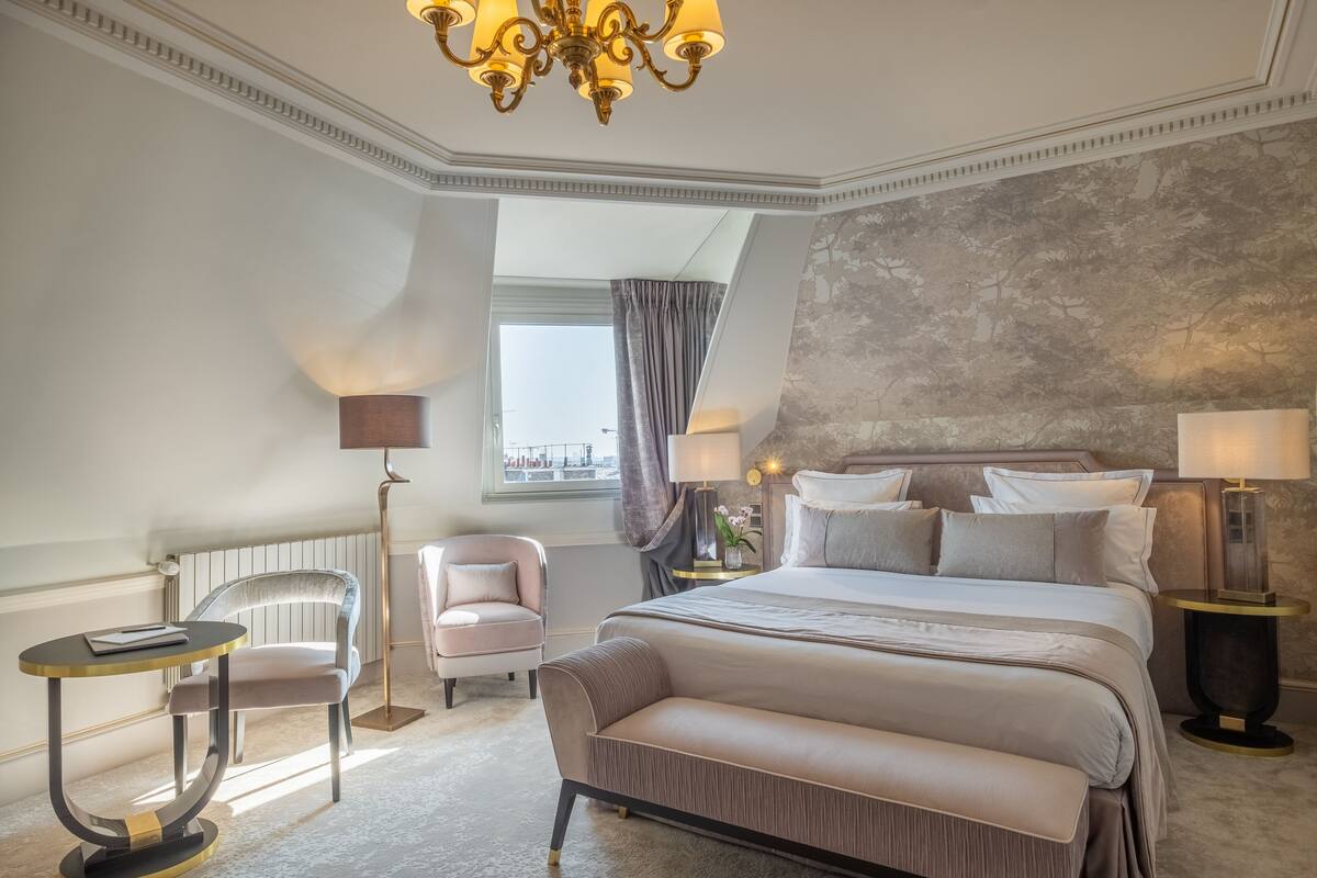 A bedroom with a large bed, a bedside table, a chair, a floor lamp, and a window with curtains.