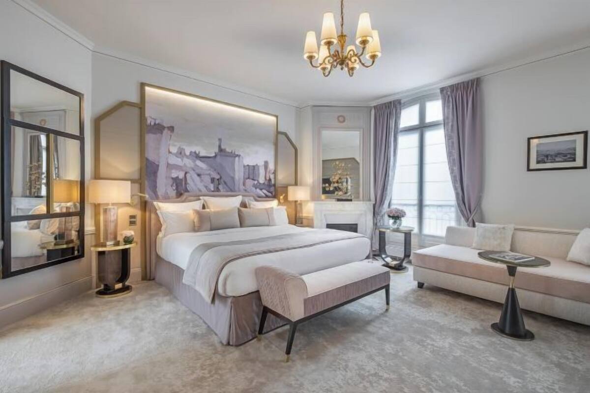 A hotel room with a large bed, a sofa, a small table, and a chandelier.
