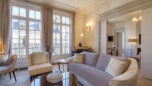 A spacious living room with a large sofa, a round coffee table, and a view of the city through large windows. - Hôtel Elysia by Inwood Hotels (Paris)