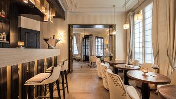 Un espace bar avec des tabourets, un comptoir et des bouteilles. On y trouve également des tables avec des chaises et, au fond, une salle à manger.