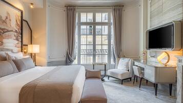 A hotel room with a large bed, a desk with a TV, a chair, and a window with curtains.