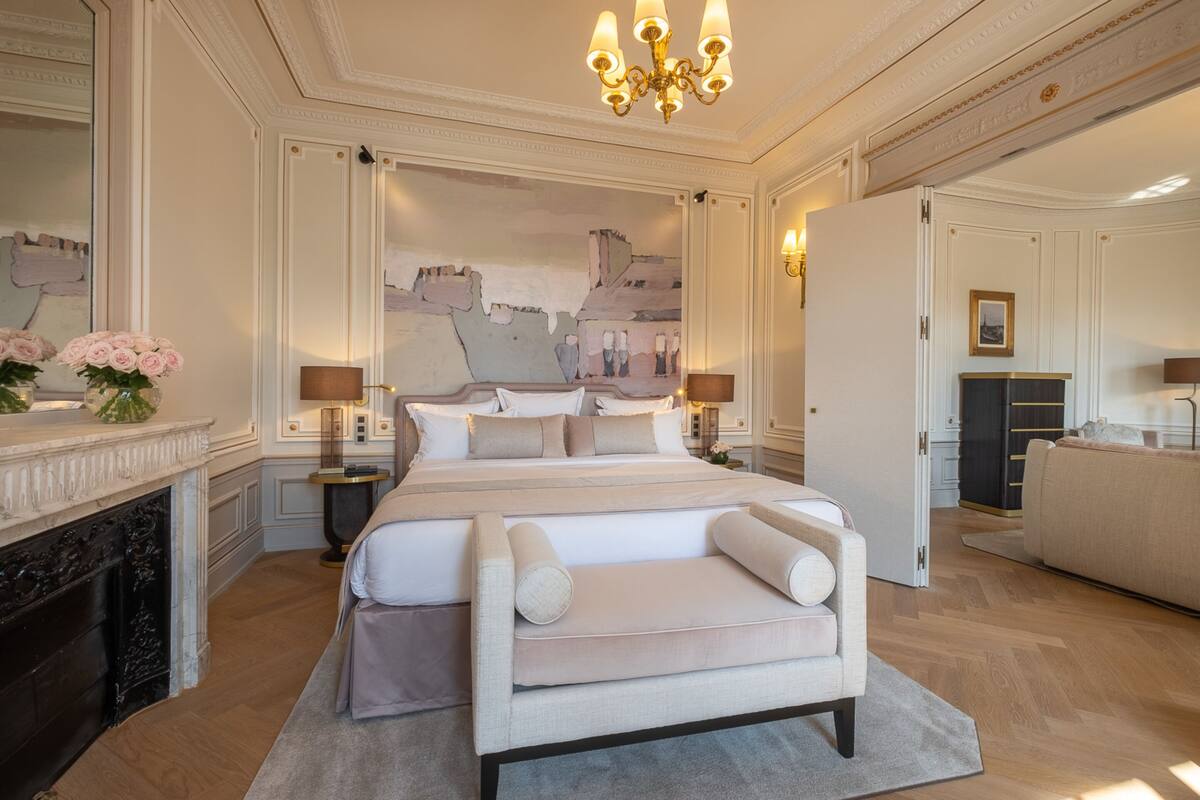 A spacious bedroom with a large bed, a chaise lounge, a fireplace, and a decorative wall mural.
