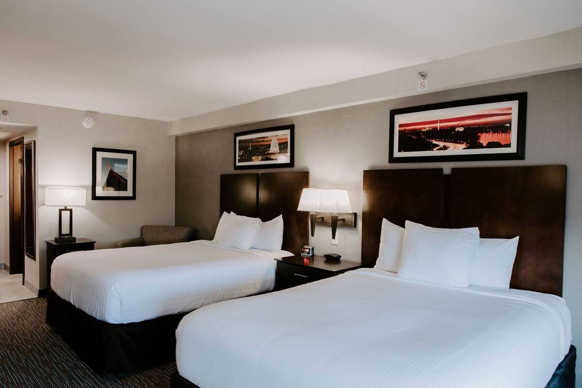 Een hotelkamer met twee bedden, een nachtkastje met een lamp, een wandklok en ingelijste foto's aan de muur.