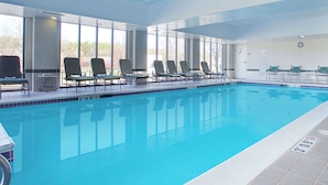 An indoor swimming pool with clear blue water, surrounded by lounge chairs and a sunshade.