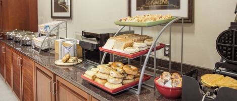 A buffet setup with various food items, including pastries and bread, on a granite countertop.