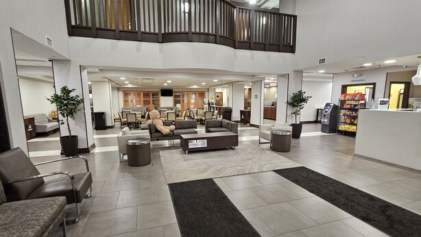 A spacious lobby with a high ceiling, a seating area with sofas and chairs, a staircase, and a kitchenette in the background.
