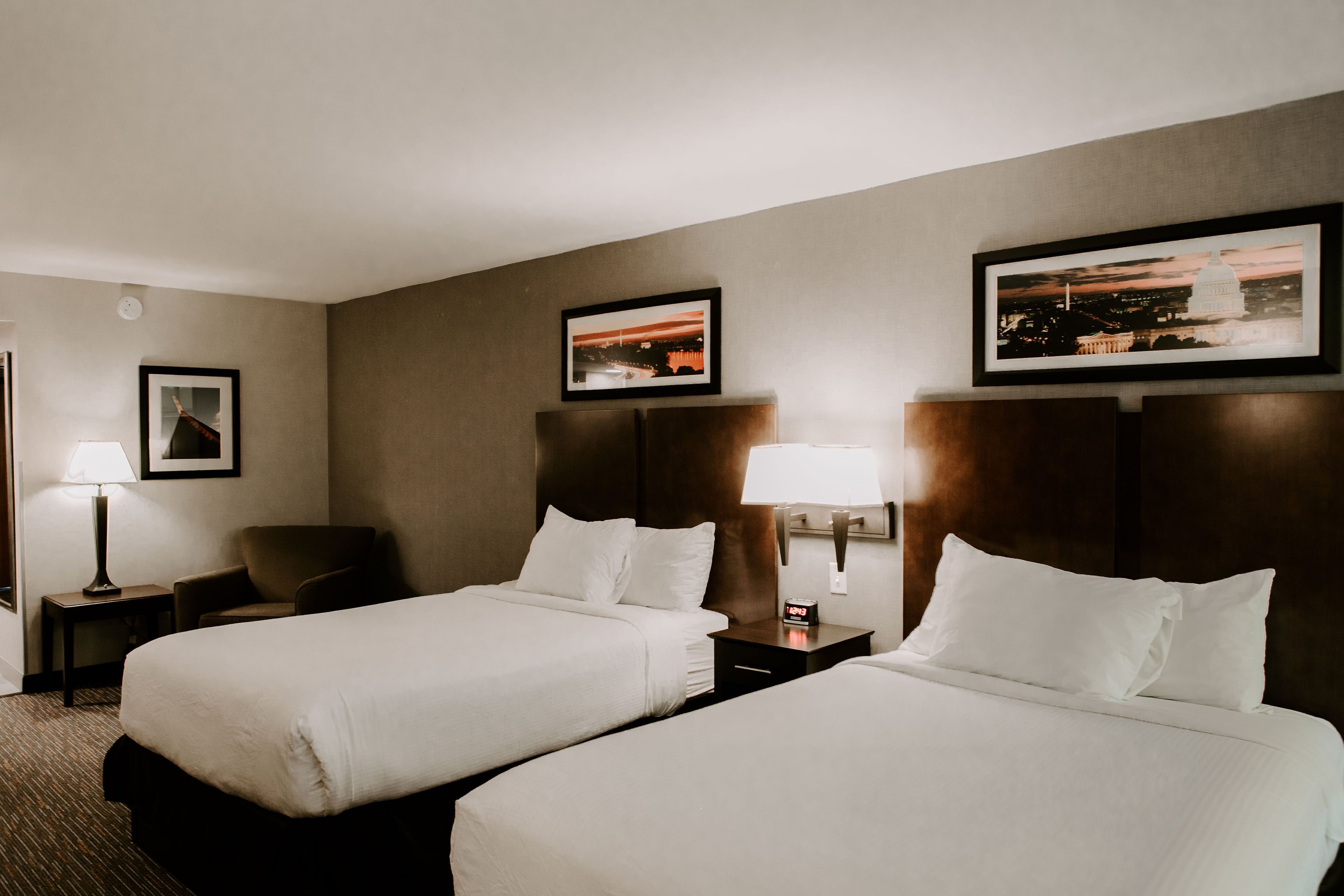 A hotel room with two beds, nightstands, a chair, and framed pictures on the wall.